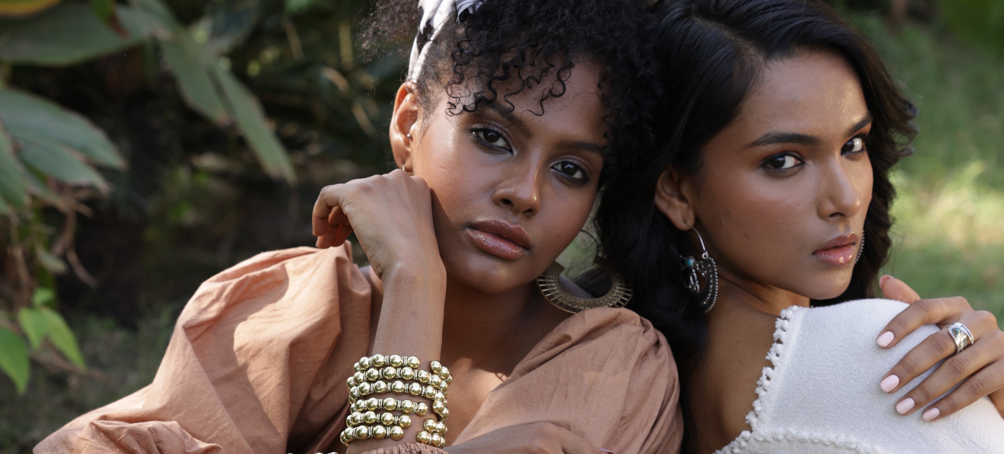Two women wearing bohemian earrings sitting outdoors with a natural background